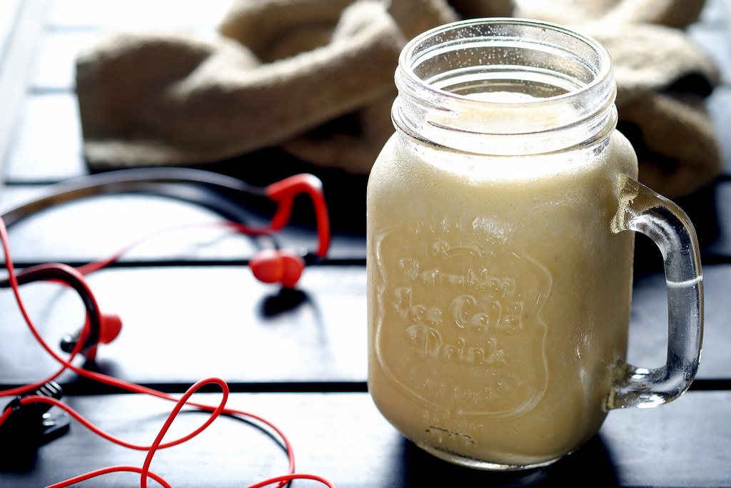 Protein shake in a glass jar with headphones beside it