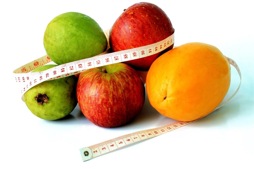Apples and an orange wrapped in a measuring tape