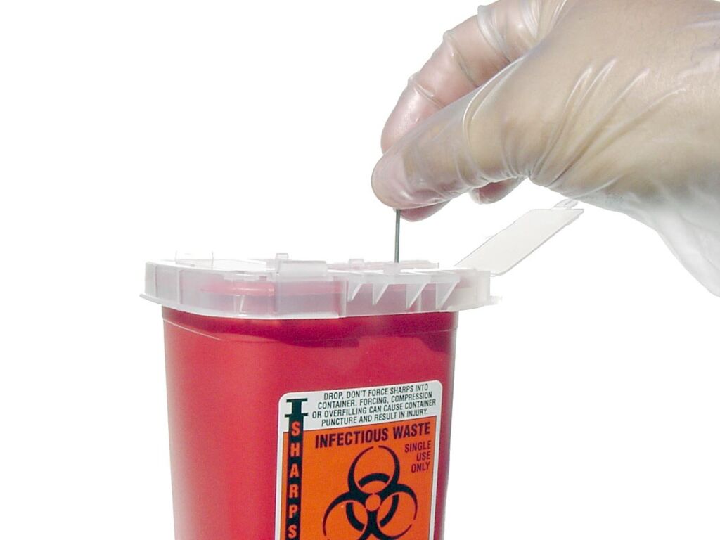 Gloved hand dropping a used syringe into a red sharps container