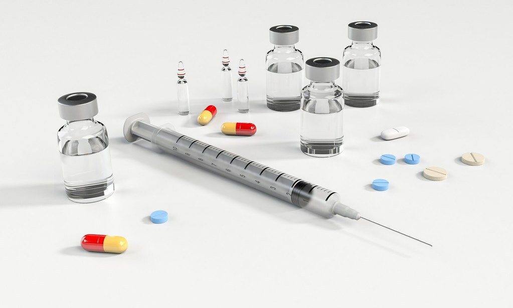 Vials, a syringe and assorted tablets laid out on white