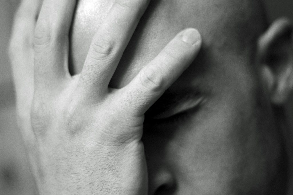 Black and white photo of a hand covering a face in stress