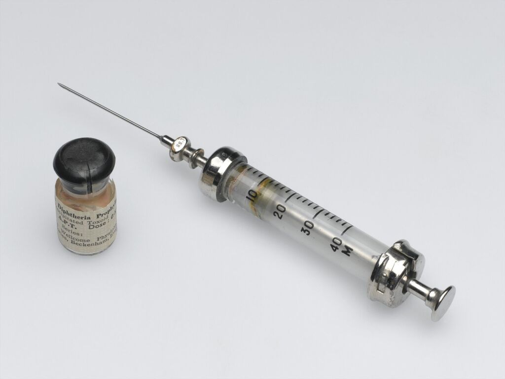 Glass hypodermic syringe next to a small medicine vial